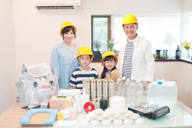 A family of four wearing protective helmets is gathered around a table, engaged in a project or activity. The well-lit space shows various items on the table, suggesting a collaborative effort or DIY project. The family appears to be enjoying the activity, sharing the experience closely together.