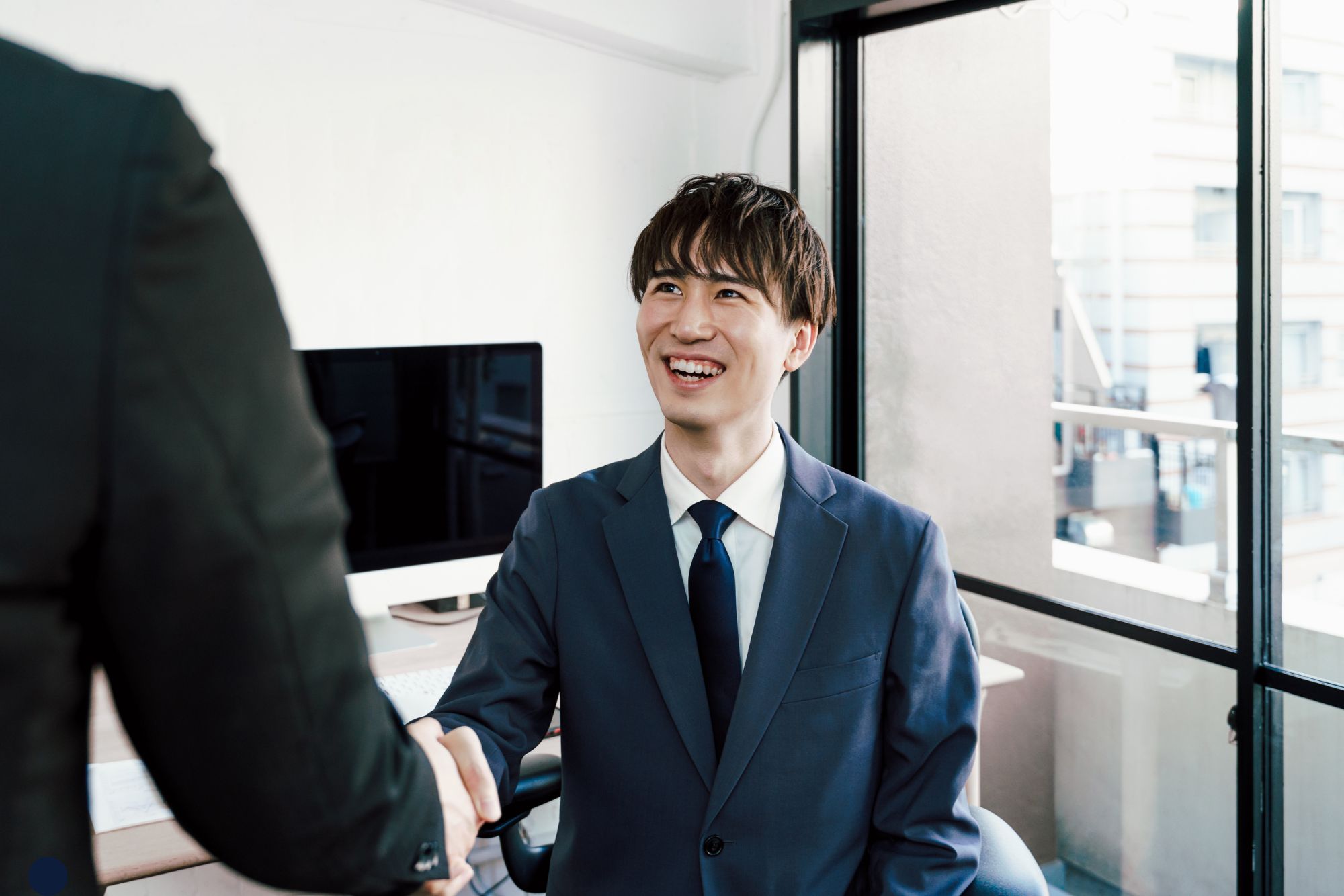 A man smiling and shaking hands with another person, expressing happiness and agreement in a professional setting.