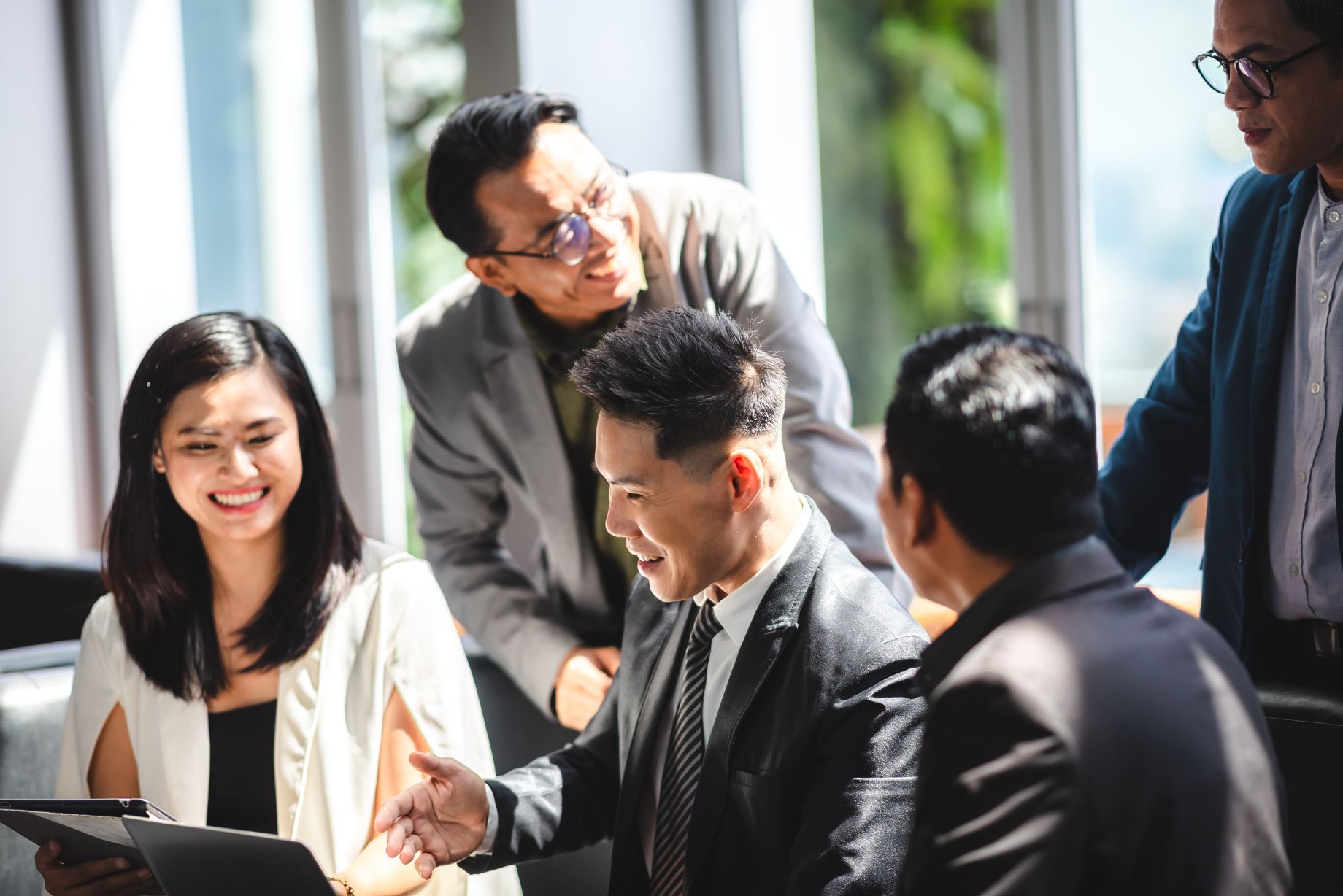A group of professionals in a business setting engaged in a meeting, with one individual extending a handshake to another, indicating a greeting or handshake is occurring. The image depicts a scene of professional interaction and collaboration.