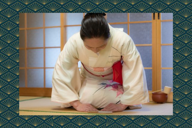 A person in traditional japanese kimono, seated in a room with tatami flooring bowing down.